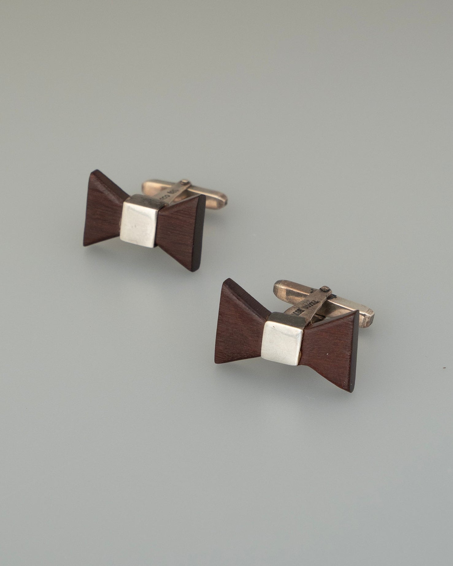 Pair of brown and silver bow-shaped cufflinks on a light gray background