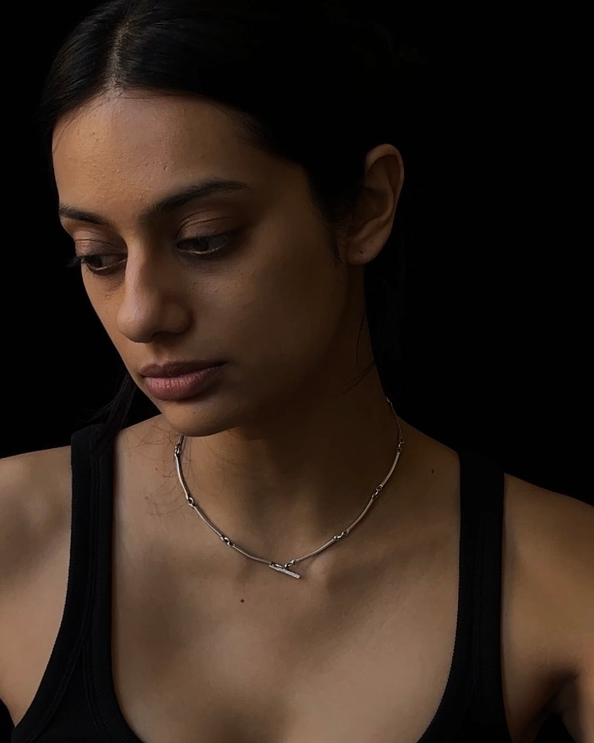 Woman wearing a delicate necklace against a dark background